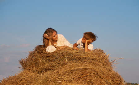 Happy children: a brother and sister lie on a haystack of freshly mown hay, against the background of an evening summer Sunny blue sky. The concept of a happy summerの写真素材