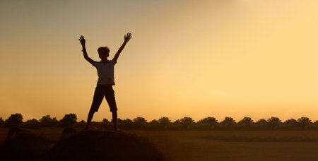 Silhouette of a happy jumping child-boy, over a haystack on the background of a field with a...