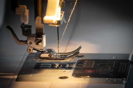 Close-up of a sewing machine and a sewing needle in the light of an incandescent lamp. The concept of industrial productionの写真素材