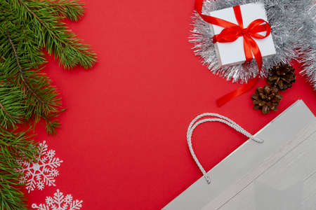 Christmas Flatley. Pine branches, white snowflakes, a gift box with a red bow and a shopping bag.The concept of new years Christmas preparations for the holiday. Red background, top view, copy space.の写真素材
