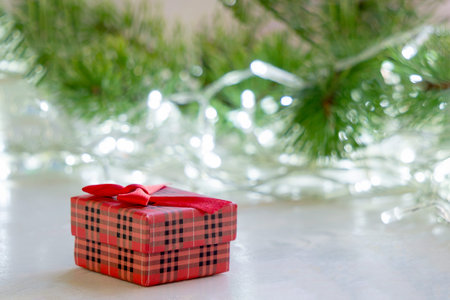 Christmas card. Red gift box on the wooden surface of the table, against a blurry background of fir...