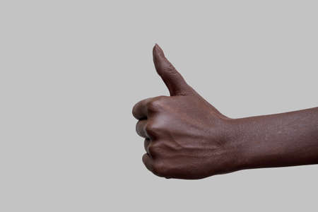 The sign of the thumb. A hand with black skin showing the like sign on a gray isolated background. Close-up, selective focus.の写真素材