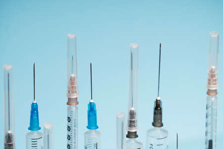 Medical syringes close-up with open and closed needles on a blue monochrome background. The concept of vaccination of the population. Selective focus, a consumable one-time tool.の写真素材