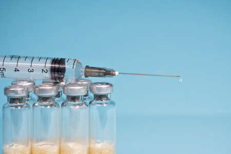 The concept of routine vaccination of the population.A medical syringe with a dose of medicine and a dripping drop lies on glass vials with the vaccine. Close-up, selective focus, copy space.の写真素材