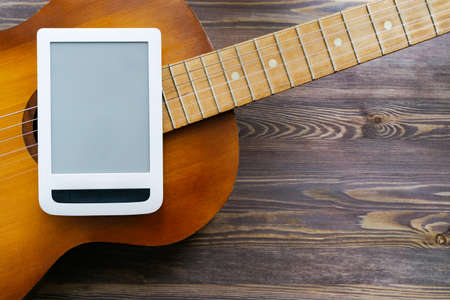 Part of a guitar, tablet on a brown wooden background. Close-up, copy space, mock up. The concept of online guitar courses.の写真素材