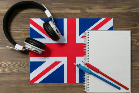 Headphones, a spiral notebook and two black-graphite pencils are lying on the flag of Great Britain....