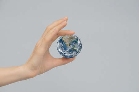 A womans hand holds the globe between two fingers. The concept of the world is in your hands. Gray isolated background, copy space.の写真素材
