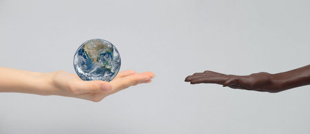 The white hand holds the earth planet in the palm of its hand and holds it out to the dark-skinned hand. The concept of equality, friendship, peace of peoples and racesの写真素材