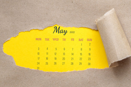 May 2021. Full-month calendar page. Hole in the paper with the edges torn off. Yellow background is...