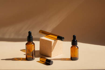 Brown glass bottles with black lids and pipettes, for cosmetics, natural oils, on beige background in the morning light. Concept of eco-skin care, 3d presentation of cosmeticsの写真素材
