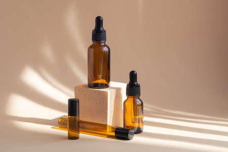 Four brown glass bottles, different shapes, on beige background with shadows from the sunlight. 3d square podium, for presentations. Concept of skin care. Natural cosmeticsの写真素材