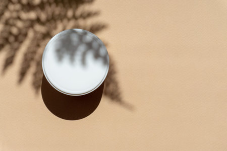 Close-up of mock-up of white jar for packaging cosmetics on beige background in rays of sunlight. Shadow of palm branch falls on object. Copy Space, flat lay. Concept of body care.の写真素材