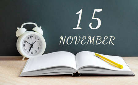 november 15.15-th day of the month, calendar date.A white alarm clock, an open notebook with blank pages, and a yellow pencil lie on the table. Autumn month, day of the year concept.の写真素材