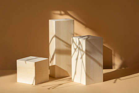 Square wooden stands, of various heights, on beige background, for demonstrating products. Shadows from branches fall on objects. Concept of 3d podium for presentation of cosmetic products.の写真素材