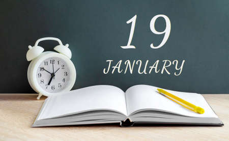 january 19.19-th day of the month, calendar date.A white alarm clock, an open notebook with blank pages, and a yellow pencil lie on the table. Winter month, day of the year concept.の写真素材