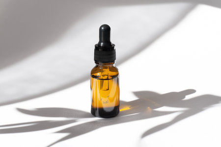 Mock-up of dropper bottle on white background. Hard shadow from tree branch falls on surface of object and table. Concept of natural cosmetics, body care, spa salonsの写真素材