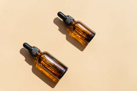 Two mock-up of dropper bottle on brown background in rays of sunlight cast a hard shadow on surface. Concept of beauty industry, flat layの写真素材