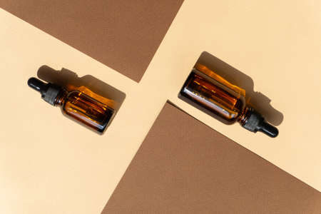 Two mockup of dropper bottle are randomly located among two sheets of brown paper. Hard shadow from objects falls on surface of beige backgroundの写真素材