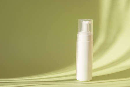 White bottle with dispenser on green background, in rays of sunlight. Mock up of packaging for cosmetic lotion, cleansing foam for washing. Concept of beauty industry.の写真素材