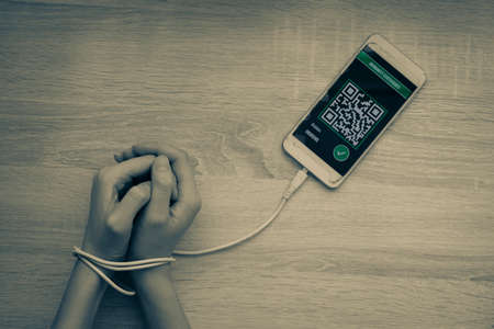 Woman's hands are connected by charger to mobile phone with an image of vaccination passport. Tinted black and white photo. Copy space, flat lay. Concept of linking to QR code.の写真素材