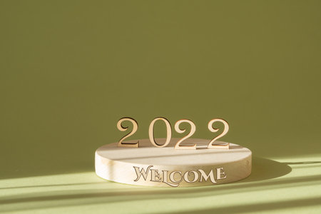 Concept of welcome to 2020. Wooden numbers on round 3-d podium with inscription, in rays of sunlight. Shadows from objects fall on green background.の写真素材