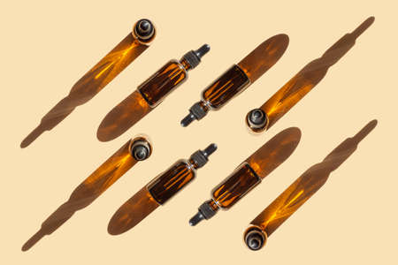 Pattern of mock-ups of glass bottles with dropper lid in sunlight on beige background. Chaotically scattered packages of essential oil, cast hard shadow on surface.の写真素材