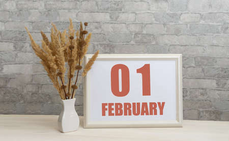 february 1. 1st day of month, calendar date. White vase with ikebana and photo frame with numbers on desktop, opposite brick wall. Concept of day of year, time planner, winter month.の写真素材