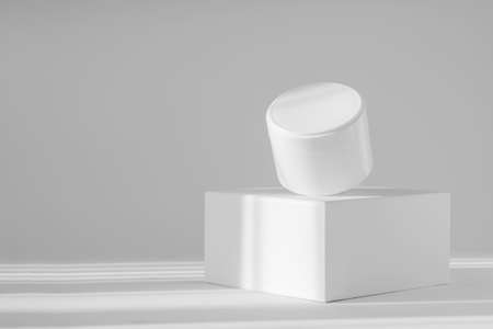 Levitating white jar of cream on square stand in rays of sunlight. White isolated background with shadows. Concept of 3d podium for demonstration of beauty products, mockup, corporate identity.の写真素材