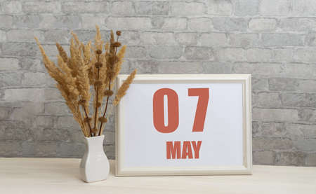 may 7. 7th day of month, calendar date. White vase with ikebana and photo frame with numbers on desktop, opposite brick wall. Concept of day of year, time planner, spring month.の写真素材