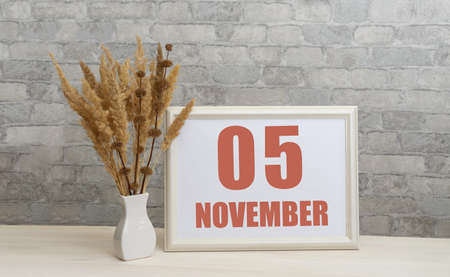 november 5. 5th day of month, calendar date. White vase with ikebana and photo frame with numbers on desktop, opposite brick wall. Concept of day of year, time planner, autumn month.の写真素材