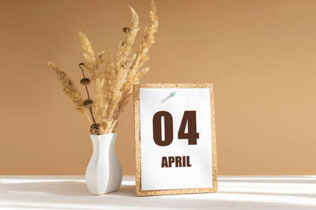 April 4. 4th day of month, calendar date.White vase with dried flowers on desktop in rays of sunlight on white-beige background. Concept of day of year, time planner, spring month.の写真素材