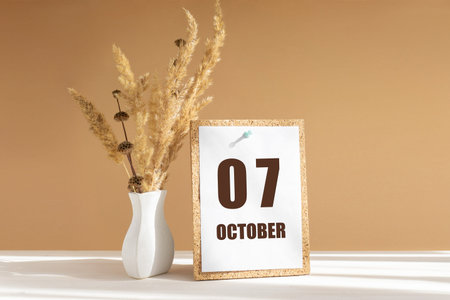 october 7. 7th day of month, calendar date.White vase with dried flowers on desktop in rays of...