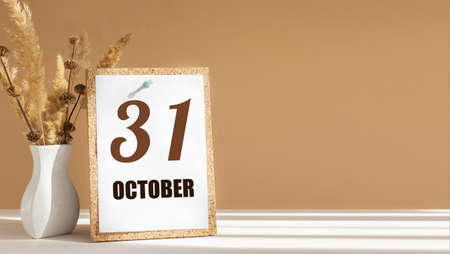 october 31. 31th day of month, calendar date.White vase with dead wood next to cork board with numbers. White-beige background with striped shadow. Concept of day of year, time planner, autumn month.の写真素材