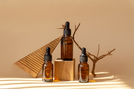 Glass bottles with serum, essential oil on wooden geometric podium next to snag in sunlight. Unmarked containers with cosmetic products on beige background. Concept of 3d podium.の写真素材
