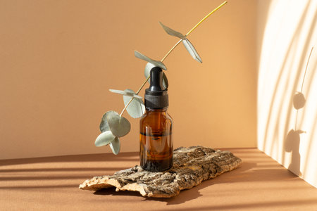 Mockup of unmarked glass bottle with moisturizing serum and levitating eucalyptus branch on brown background. Cosmetic container with dropper for medicines, oils on stand made of piece of bark.の写真素材