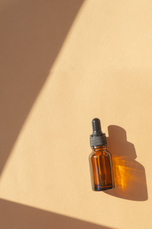 Top view of essential oil in amber glass bottle with dropper lid on brown background with geometric hard shadow. Serum for care of women's skin close-up in rays of sunlight. Flat lay, copy space.の写真素材