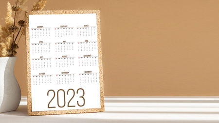 Calendar for new year 2023 for planners and reminders on desktop next to white vase. Close-up, white-brown background with shadow from rays of sun. concept mockup.の写真素材