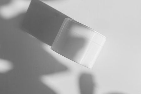 Face cream in white jar on light background with shadows from leaves. Mockup of clean package for cosmetics in rays of sunlight. Close-up, flat lay, copy space.Top viewの写真素材