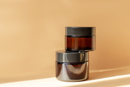 Amber glass cream jars on brown background with shadow in sunlight. Stylish product appearance, mockup, brandingの写真素材