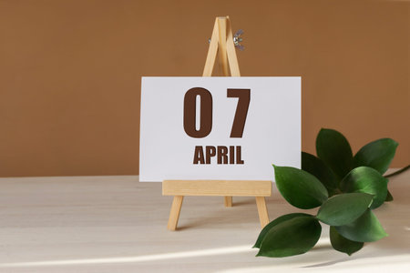 April 7th. Day 7 of month, Calendar date. Green branch, easel with the date and month on desktop. Close-up, brown background. Spring month, day of year concept.の写真素材