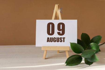 August 9th. Day 9 of month, Calendar date. Green branch, easel with the date and month on desktop....
