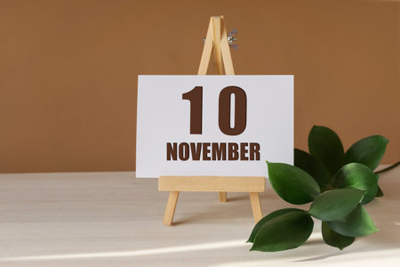 November 10th. Day 10 of month, Calendar date. Green branch, easel with the date and month on desktop. Close-up, brown background. Autumn month, day of year concept.の写真素材