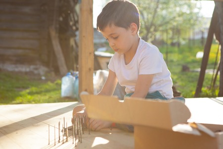 Boy hammers nails with a hammer in a wooden boardの写真素材