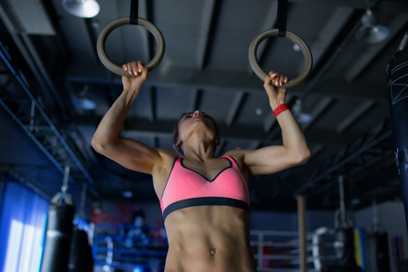 Young woman doing a pullup ongymnastic rings, in the gymの写真素材