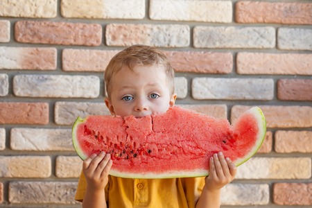 Funny kid eating watermelon indoors, focus on eyes.の写真素材