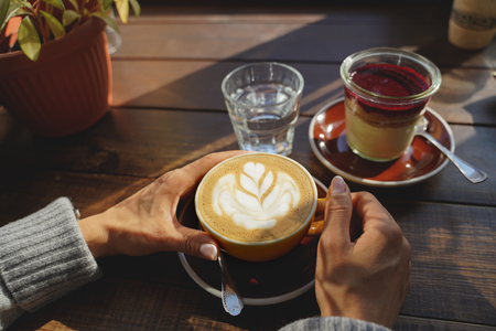 close-up of womans hands with a cup of coffee cake, the suns rays shine through a window in the cafe. Hand and cup coffee.の写真素材