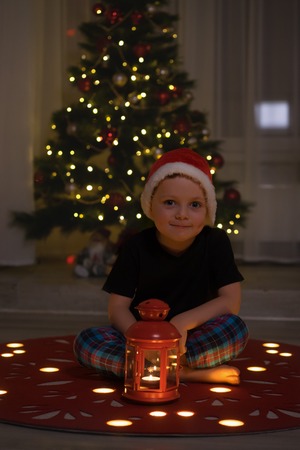 the little boy to Santas red hat sitting near the Christmas treeの写真素材