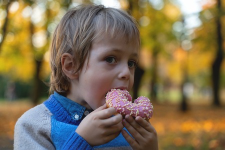 Young caucasian boy 5 years old eating donut outdoors closeup. Childhood.の写真素材