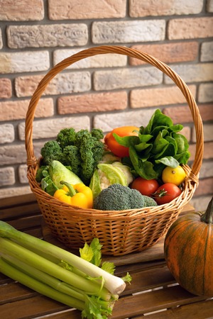 Healthy fresh vegetables and fruits in willow basket on wooden backgroundの写真素材