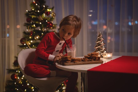 adorable happy boy in santa hat holding baking tray with ginger cookies and smiling at cameraの写真素材